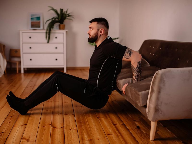 A focused man performing a bodyweight exercise on a dark floor.